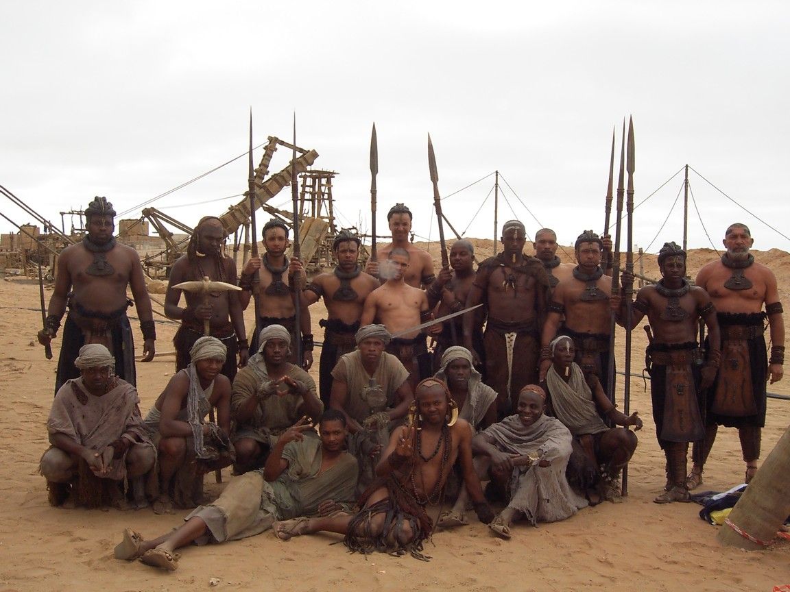Performers in warrior costume with spears on a desert set