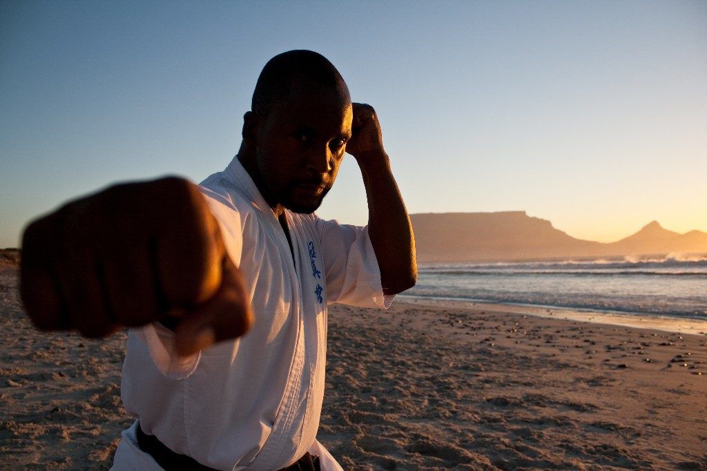 Sensei San Ndlovu throwing a punch on the beach at sunset, Table Mountain behind