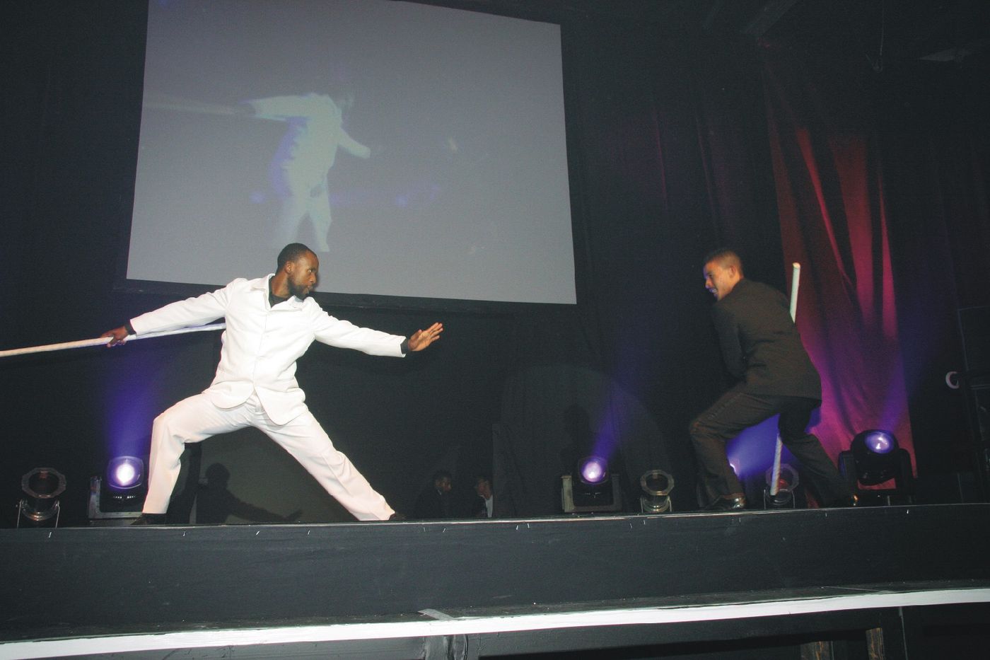 Sensei San Ndlovu performing a sword sequence on a lit stage at a corporate event