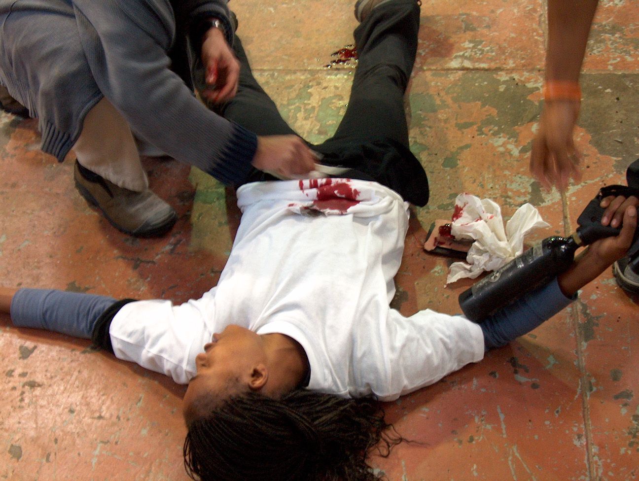 A trainee lying still with a fake blood squib on a white shirt