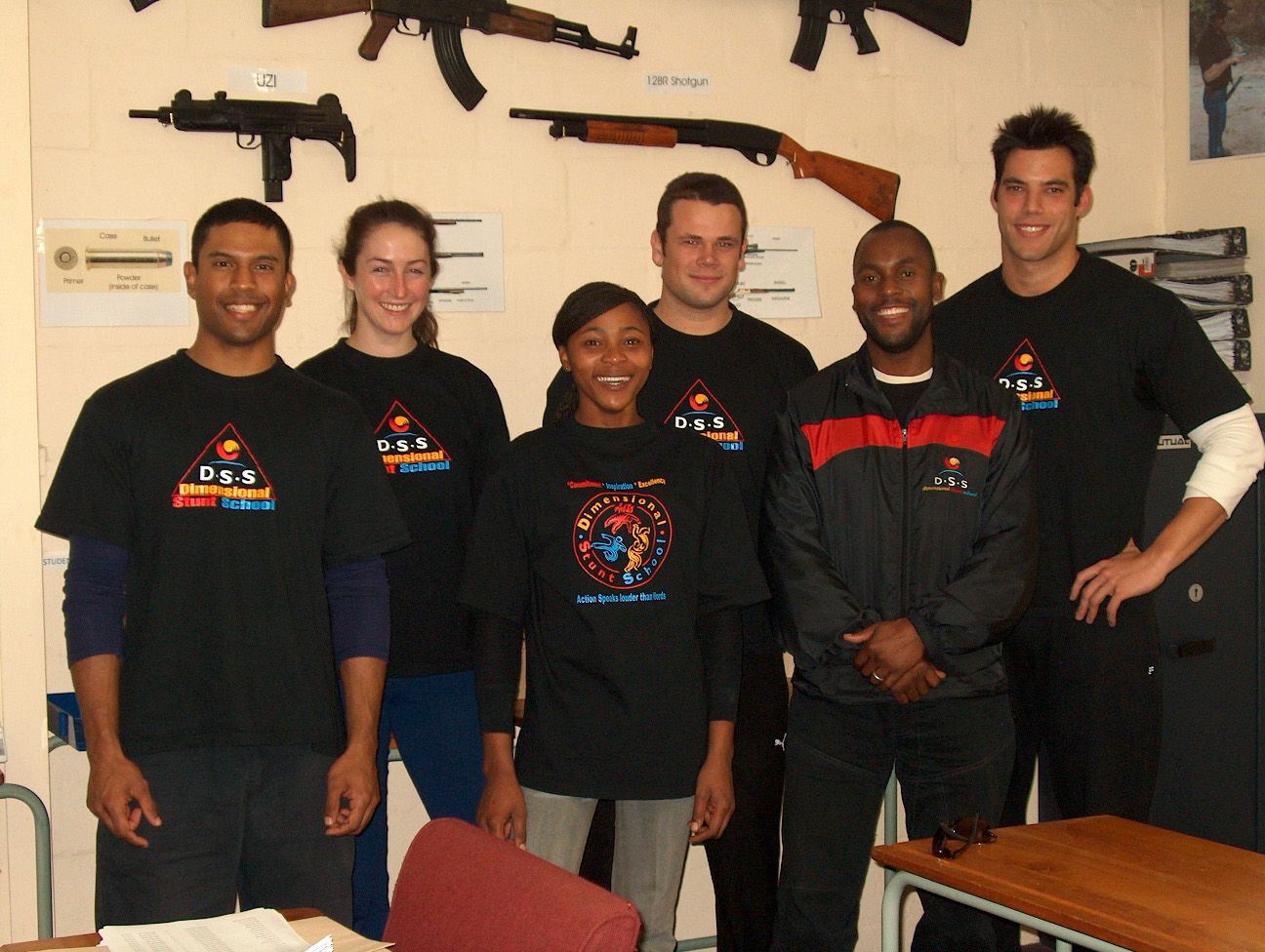 Sensei San Ndlovu with trainees in the weapons room, firearms on the wall behind