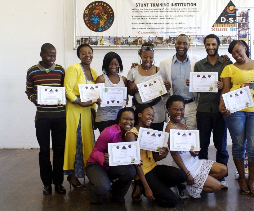 A graduating class holding their certificates in front of DSS banners