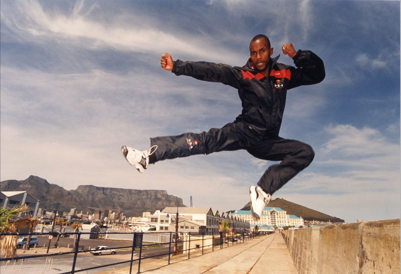 Sensei San Ndlovu in a flying side kick above the Cape Town waterfront, Table Mountain behind