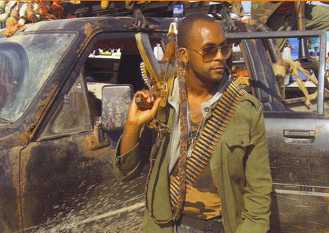 Sensei San Ndlovu on set as an armed hitman, ammunition belt over his shoulder