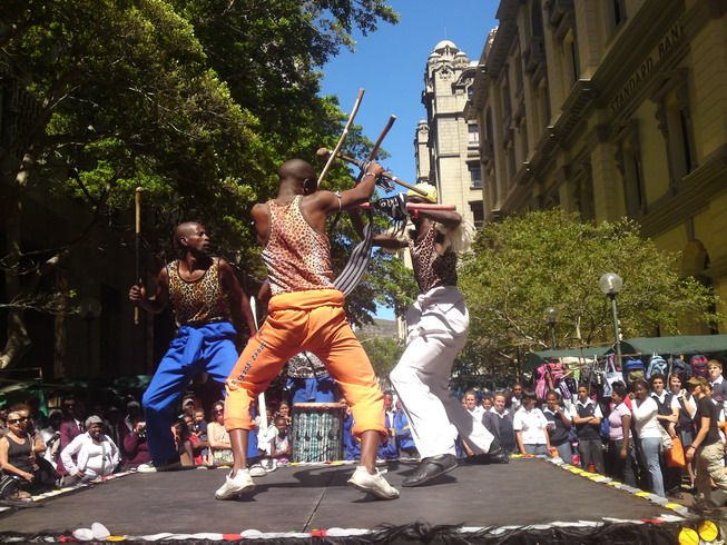 Stick fighters in leopard-print costumes clash on an outdoor stage in the city centre