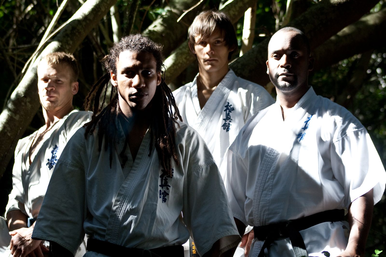 Sensei San Ndlovu with two fellow Kyokushin karateka in white gis and black belts, under trees