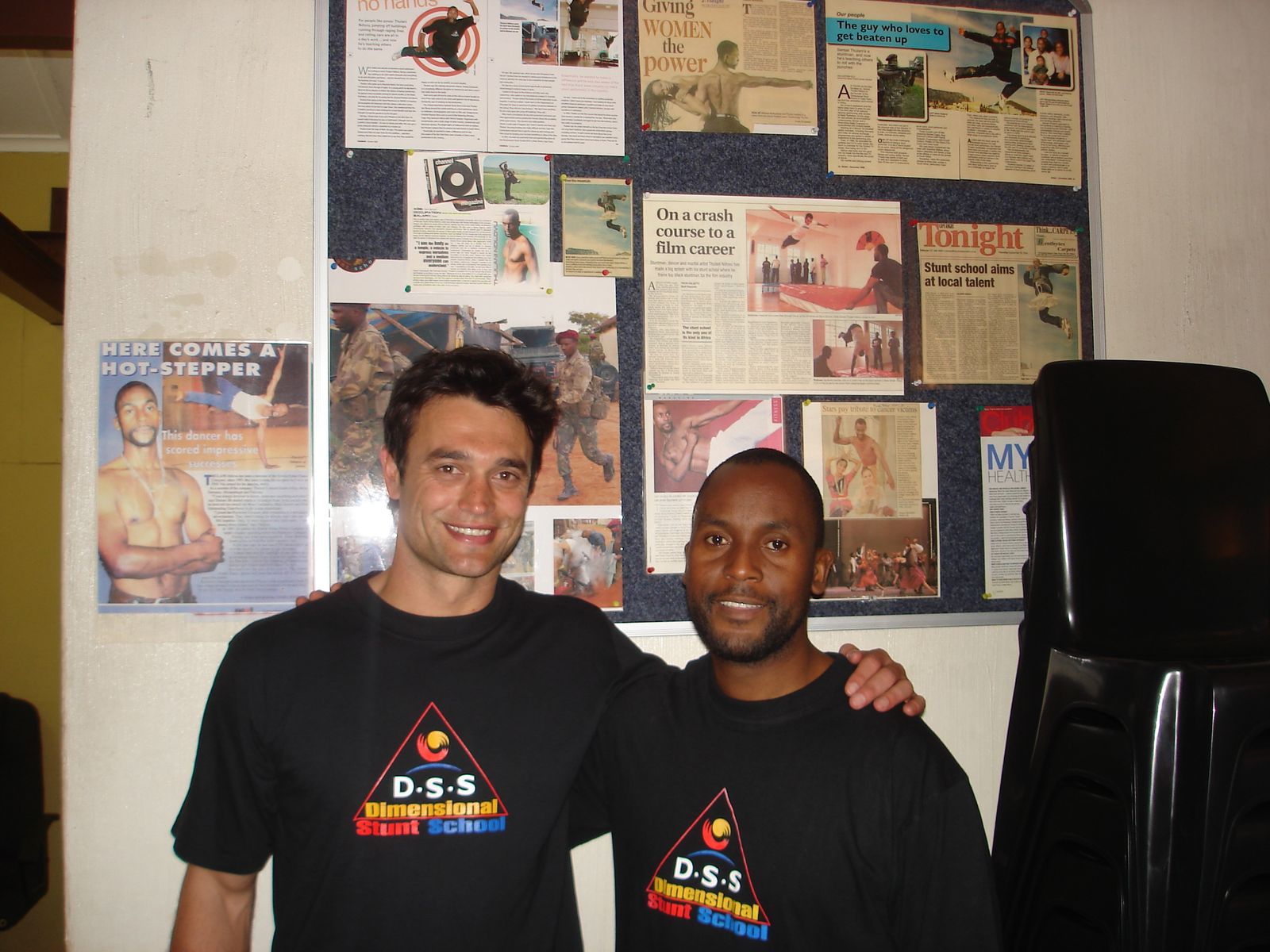 Sensei San Ndlovu with the Pasella presenter in front of a wall of press clippings