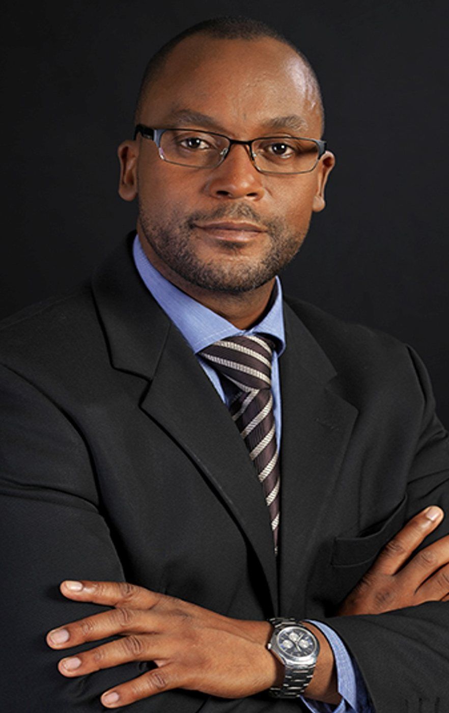 Studio portrait of Sensei San Ndlovu in a dark suit, arms folded